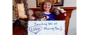 Picture of teacher holding stuffed animals and a sign that says, "sending lots of love and missing you!"